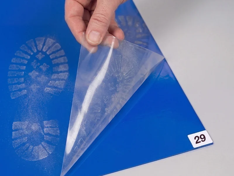 Hand peeling a used sheet from a blue sticky mat to reveal fresh adhesive layer 29